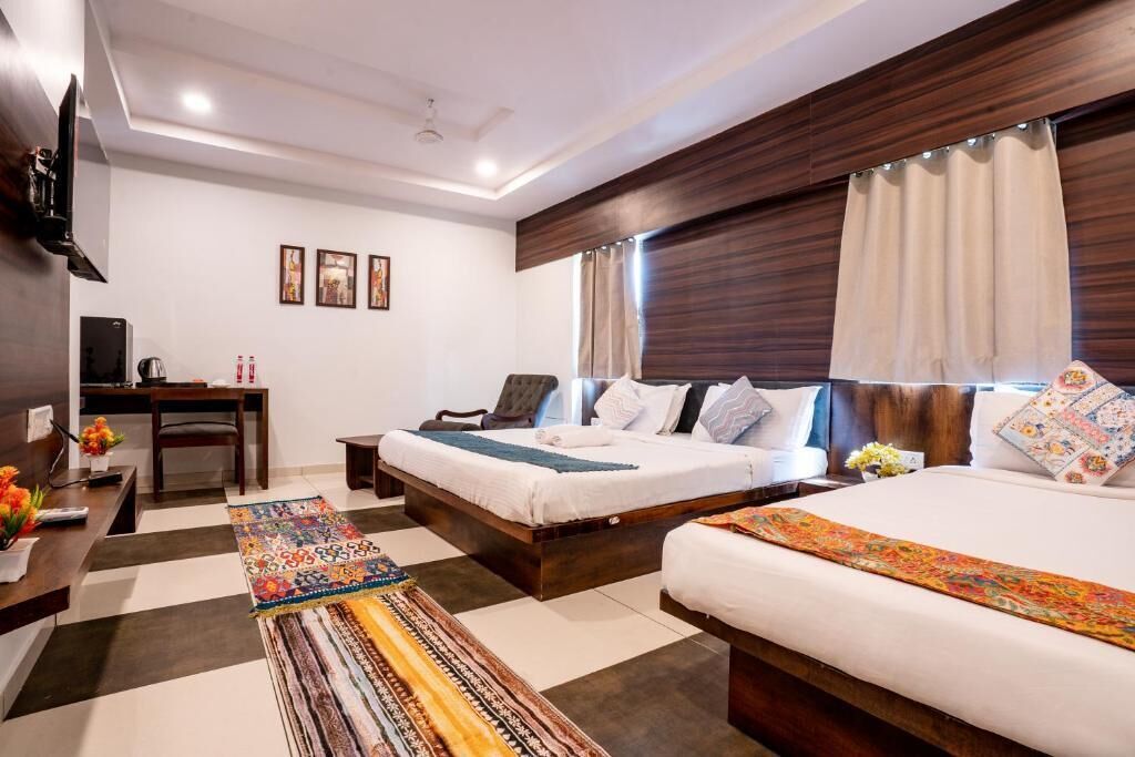 A hotel room with two beds, a desk, a TV, and a large window with curtains.