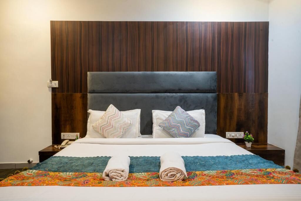 Una cama con cabecera de madera, dos almohadas, un edredón y dos toallas enrolladas.