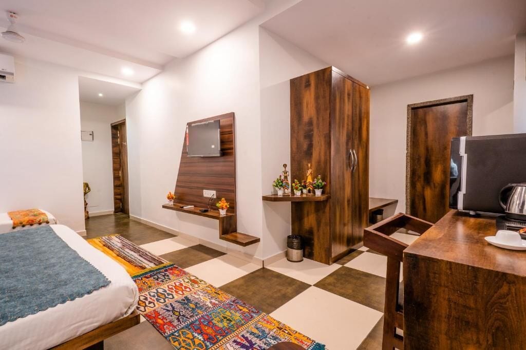 Quarto moderno com cama, televisão na parede, guarda-roupa, escrivaninha com cadeira e um tapete colorido.