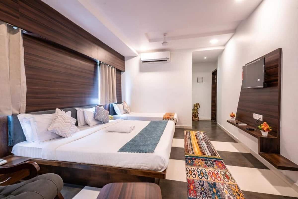 A modern hotel room with a large bed, a desk, a chair, a TV, and an air conditioning unit.