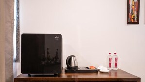 Una habitación con un refrigerador negro, una tetera, una bandeja con tazas y una caja, y dos botellas de agua sobre una mesa de madera.