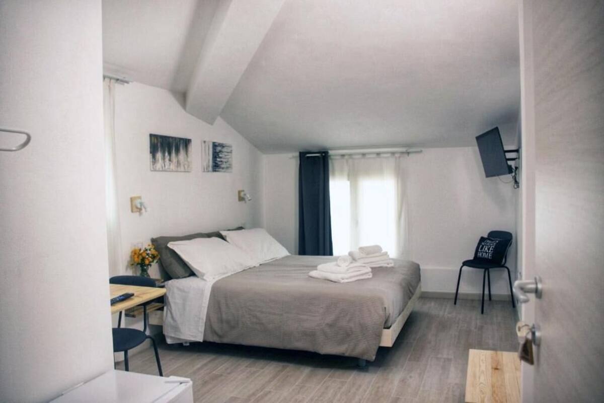 A bedroom with a bed, a desk, a chair, a TV, and a window with curtains.