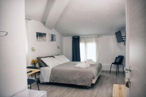 A bedroom with a bed, a desk, a chair, a TV, and a window with curtains.