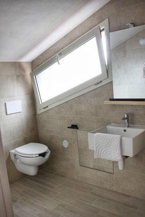 A bathroom with a toilet, a sink, a mirror, and a window.