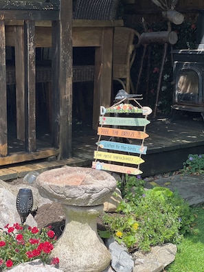 Een rustieke buitenomgeving met een houten constructie, een stenen vogelbad en een bewegwijzer met houten borden.