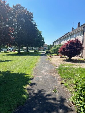Ein Weg führt an einer Reihe Häuser vorbei, im Vordergrund steht ein Baum und ein Busch.
