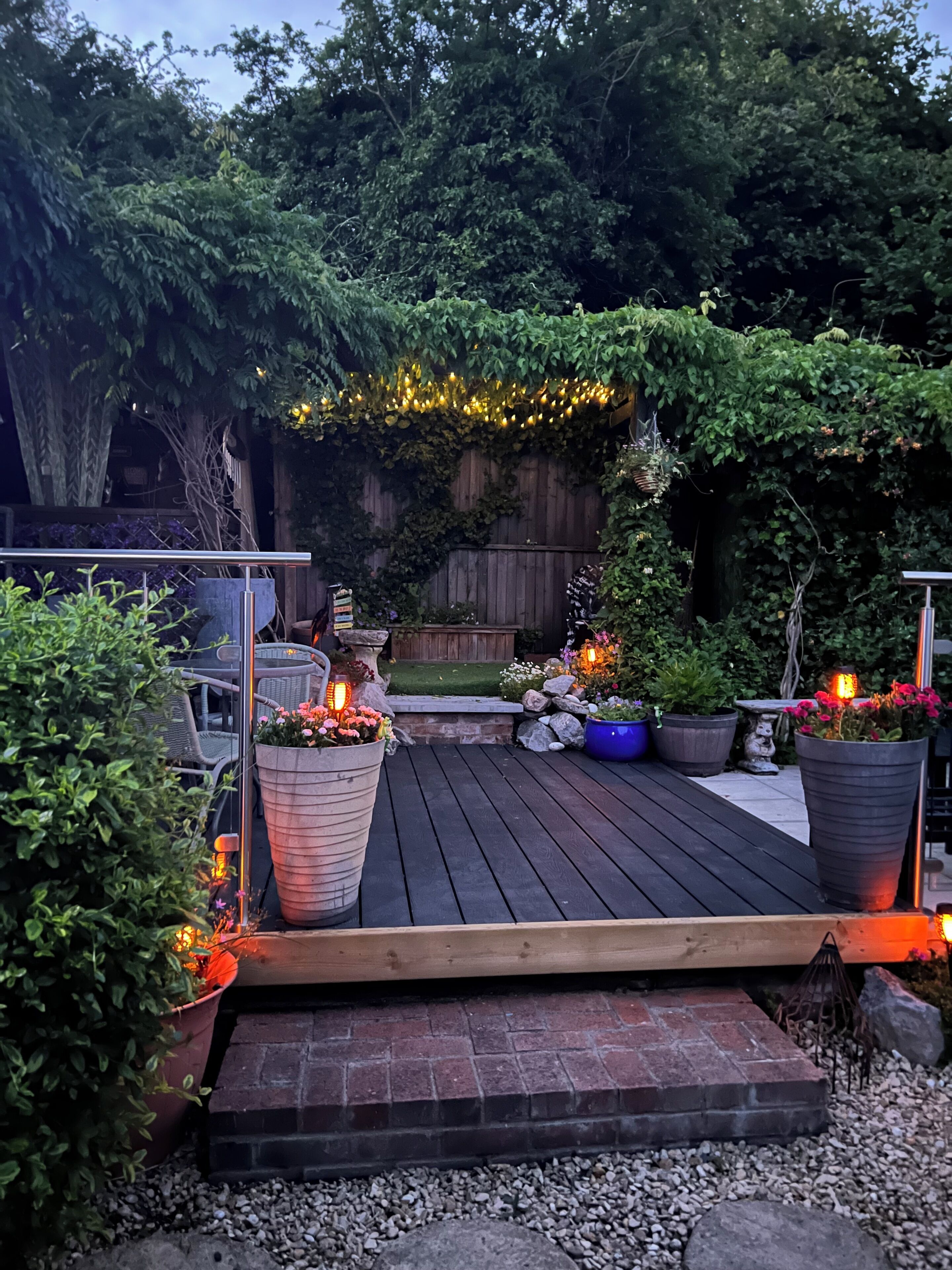 A wooden deck with potted plants and outdoor lighting.