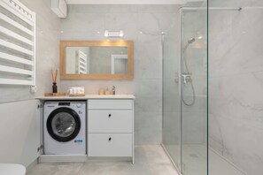Un baño moderno con lavadora, cabina de ducha de vidrio, espejo y tocador con lavabo.