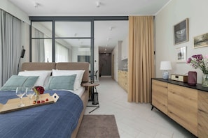 Een moderne hotelkamer met een groot bed, een nachtkastje met lamp, een dressoir en uitzicht door een glazen deur.