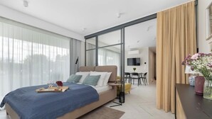 A modern hotel room with a large bed, a desk, a chair, and a view through a glass door. - Air Conditioned Apartment | Pool | Terrace | Close to Lake and Beach (Mielno)