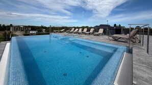 A rectangular swimming pool with clear blue water, surrounded by lounge chairs and a covered area with a metal roof. - Air Conditioned Apartment | Pool | Terrace | Close to Lake and Beach (Mielno)