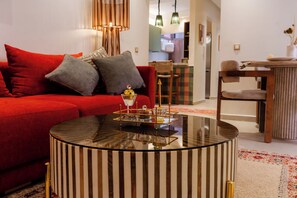 A living room with a red sofa, a striped coffee table, and a dining area with a wooden table and chairs. - Gigi Apartment with Pool & Parking (Marrakesh)