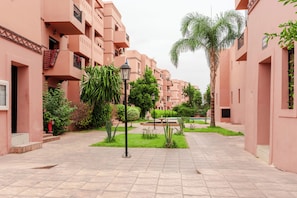 A courtyard with pink buildings, a central fountain, and a palm tree. - Gigi Apartment with Pool & Parking (Marrakesh)