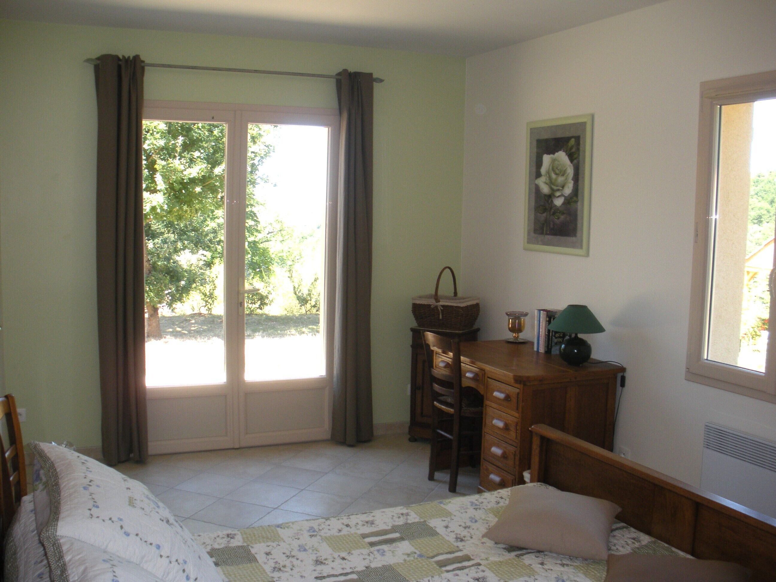 Een slaapkamer met een bed, een bureau, een stoel, een raam en een deur.