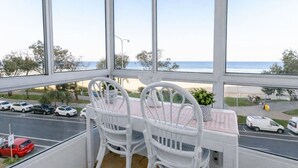 En balkon med to hvide fletstole, et lille bord og udsigt til stranden og biler.
