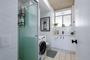 Ein Waschraum mit einer Waschmaschine, einem Wäscheständer und einem kleinen Fenster mit Pflanzen.