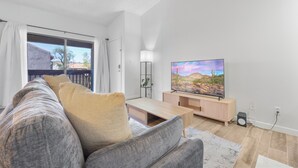 A modern living room with a sofa, TV, and a view of a balcony. - Central Mesa 1BR Close to Hospitals (Mesa)