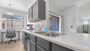 A modern kitchen with a large island, double sink, and a dining area with a chair and table. - Central Mesa 1BR Close to Hospitals (Mesa)