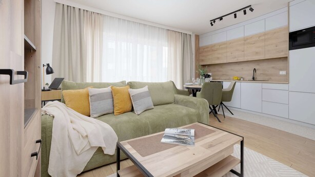 Ein modernes Wohnzimmer mit Sofa, Couchtisch und einer Küchenzeile im Hintergrund.
