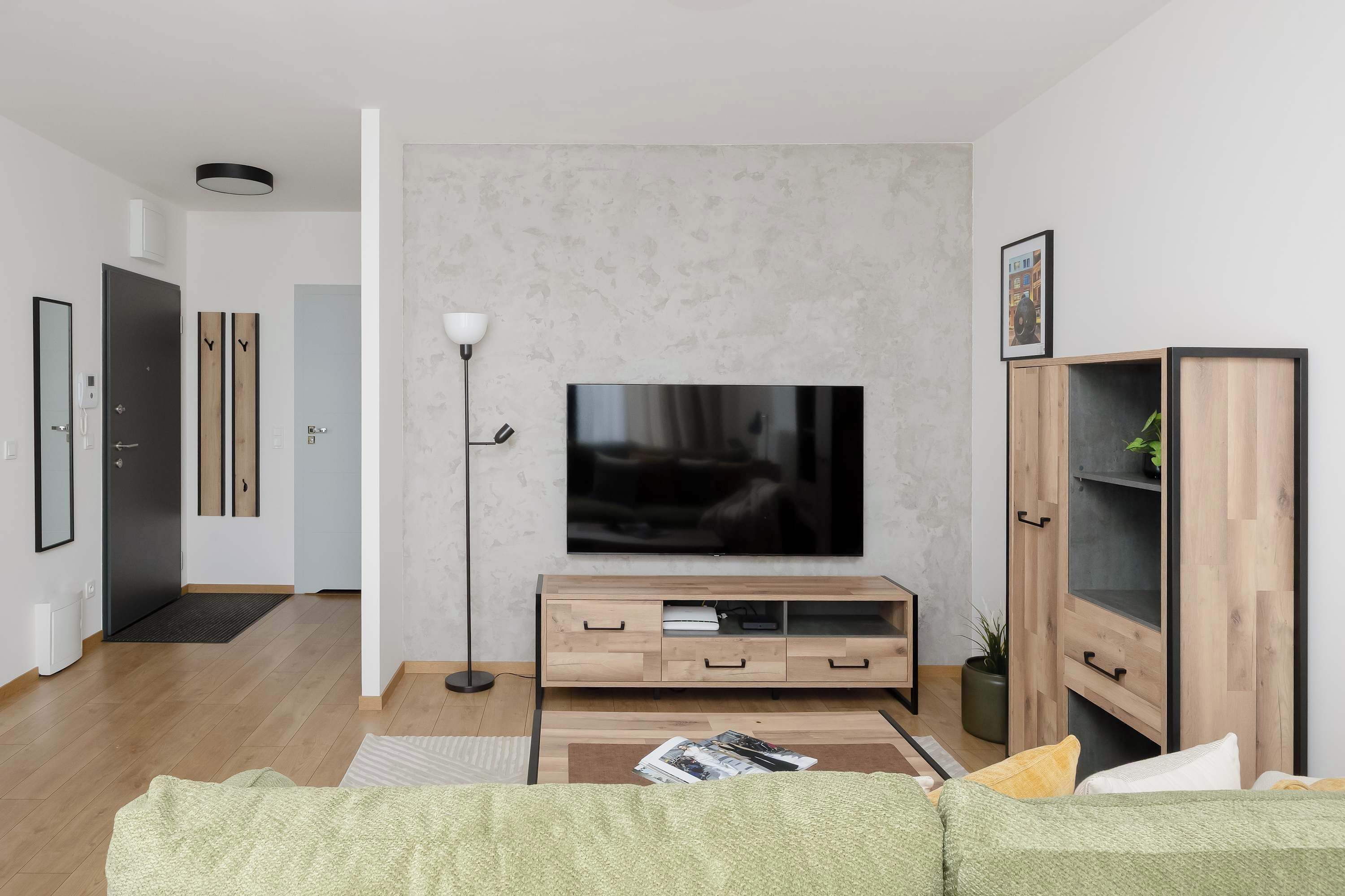 Un salon moderne avec un téléviseur à écran plat, un meuble de rangement en bois et un canapé vert.