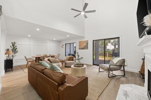 A spacious living room with a brown sofa, round coffee table, and a ceiling fan. - Steps to Beach Access | Gated Holiday Isle Townhome (Destin)