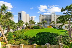 A hotel with a green lawn, palm trees, and modern buildings in the background. - Steps to Beach Access | Gated Holiday Isle Townhome (Destin)