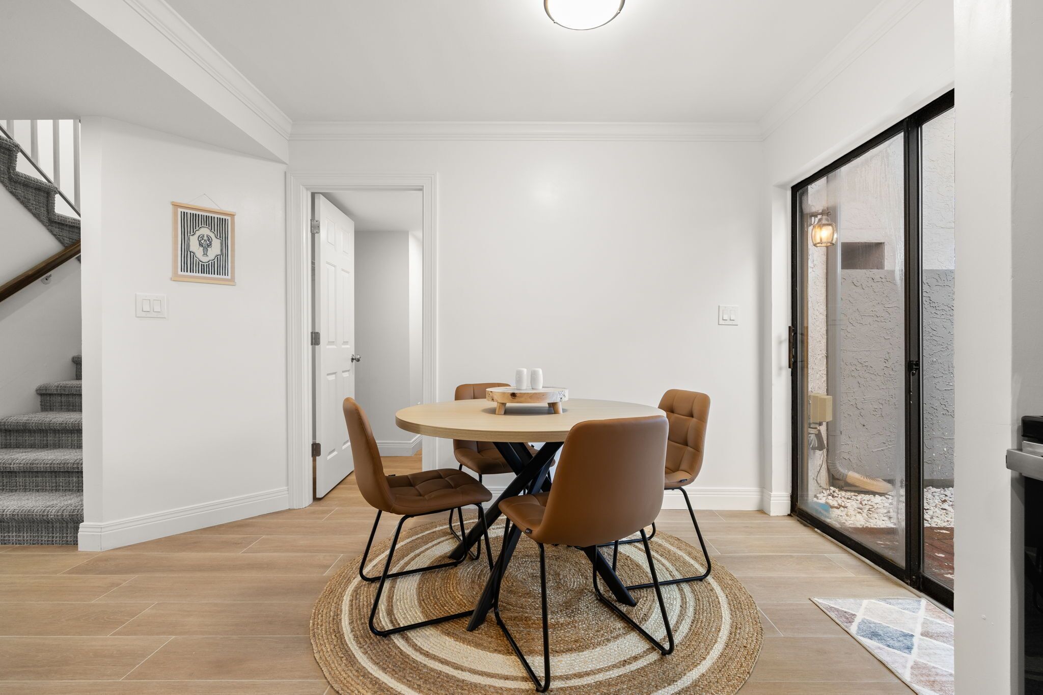 Un comedor con una mesa redonda, seis sillas, un tapete y una escalera al fondo.