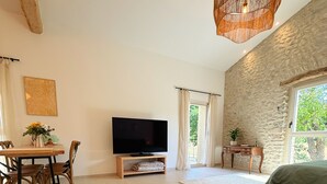 A living room with a TV, wooden coffee table, dining table with chairs, stone wall, and a hanging light fixture. - ⭐​ The Colibris Loft ⭐​ (Mirabel-et-Blacons)