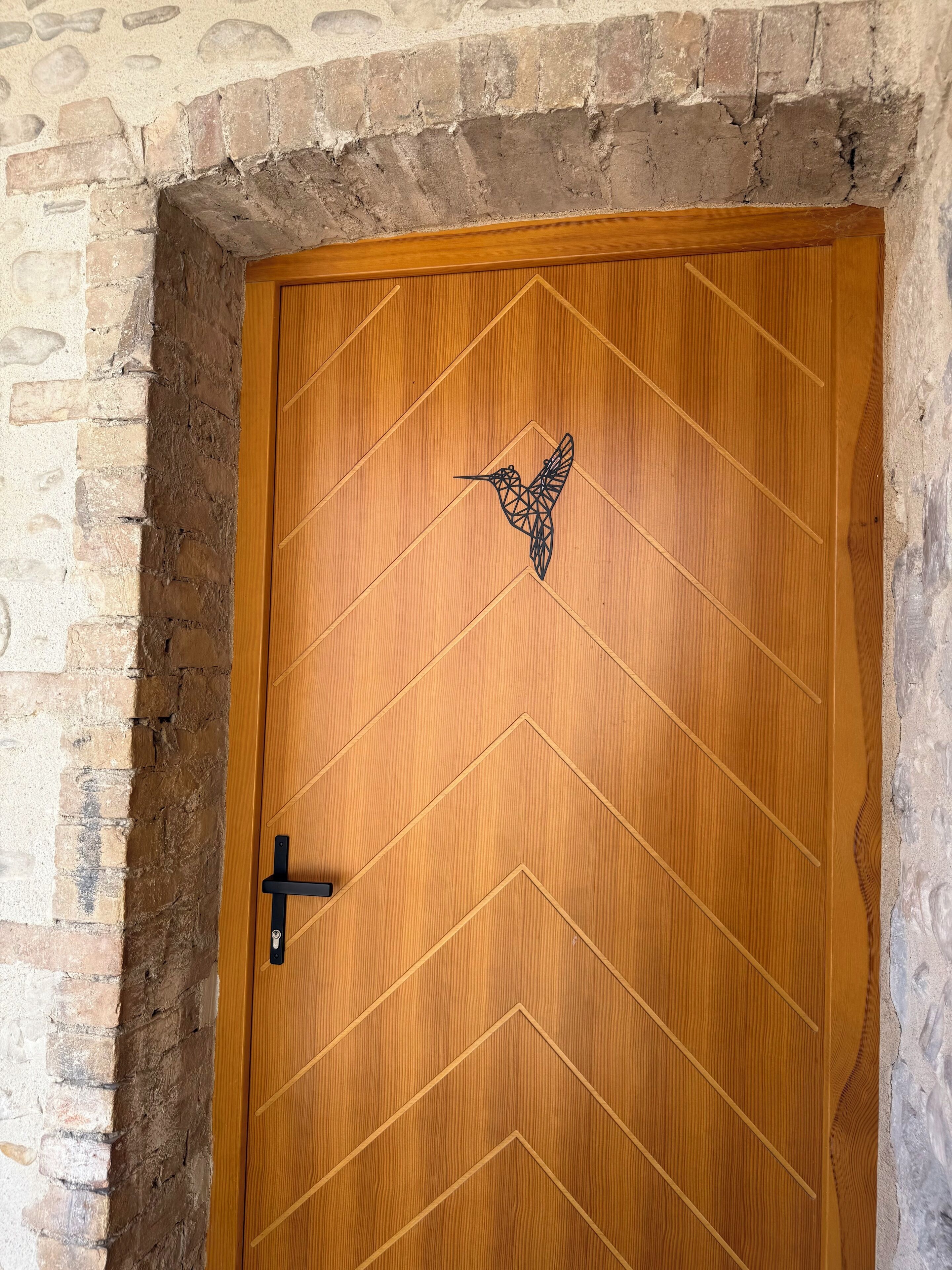 A wooden door with a geometric pattern and a bird design, set in a brick wall.