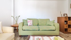 Een woonkamer met een groene bank, een bijzettafeltje met een vaas en een houten kast.