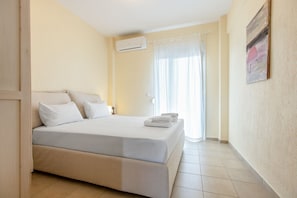 Ein Hotelzimmer mit Bett, Nachttisch, Klimaanlage, einem Fenster mit Vorhängen und einem Bild an der Wand.
