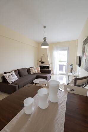 Ein modernes Wohnzimmer mit einem Ecksofa, einem runden Couchtisch und einem Esstisch mit weißen Stühlen.