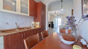 A kitchen with wooden cabinets, a dining table, chairs, and a vase with flowers. - Nerea Beach House by Rentals Pro - Mouries Halkidiki (Mouries)