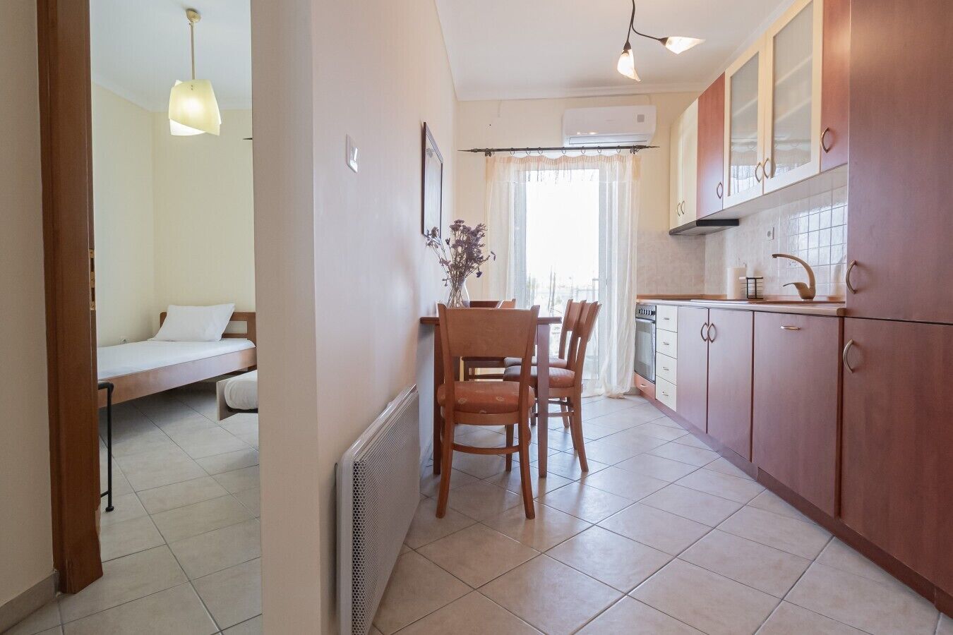 Een compacte keuken met een eethoek, een bed in de aangrenzende kamer, en een radiator.