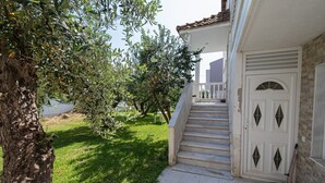 A house with a white exterior, a set of stairs leading to a door with diamond-shaped windows, and a tree in the foreground. - Nerea Beach House by Rentals Pro - Mouries Halkidiki (Mouries)