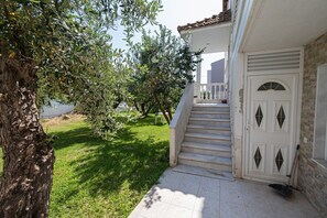 A house with a white exterior, a set of stairs leading to a door with diamond-shaped windows, and a tree in the foreground. - Nerea Beach House by Rentals Pro - Mouries Halkidiki (Mouries)