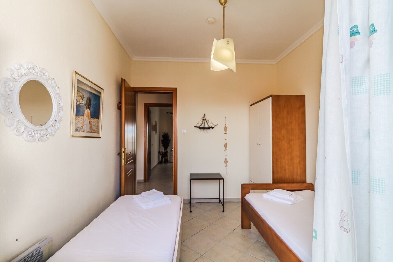 Une chambre avec deux lits, un miroir, un tableau, un lustre et une porte donnant sur une autre pièce.