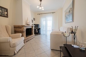 A living room with a fireplace, two armchairs, a sofa, a TV, and a painting on the wall. - Nerea Beach House by Rentals Pro - Mouries Halkidiki (Mouries)