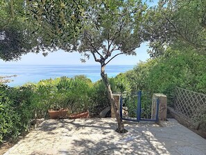 Ein gepflasterter Weg führt zu einem Tor mit Blick auf das Meer.