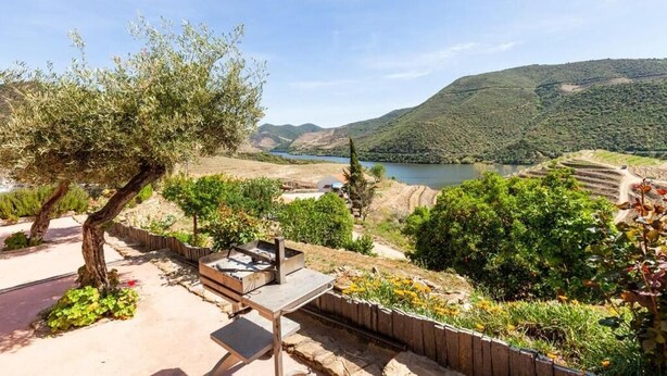 A scenic outdoor area with a table and chairs, surrounded by greenery and a view of a lake and hills. - Quinta das Amendoeiras (Carrazeda de Ansiaes)