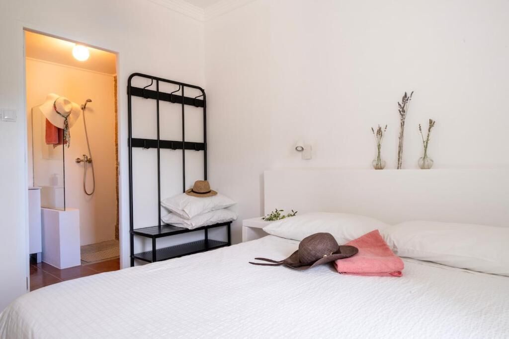 A bedroom with a bed, a nightstand, a black metal rack, and a wall-mounted shelf with decorative items.