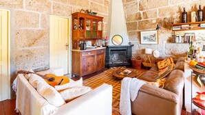 A cozy living room with a stone wall, a fireplace, a wooden cabinet, a sofa, a coffee table, and a guitar. - Quinta das Amendoeiras (Carrazeda de Ansiaes)
