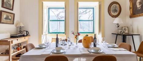 A dining room with a table set for four, two windows, a small side table, and a wall-mounted lamp.