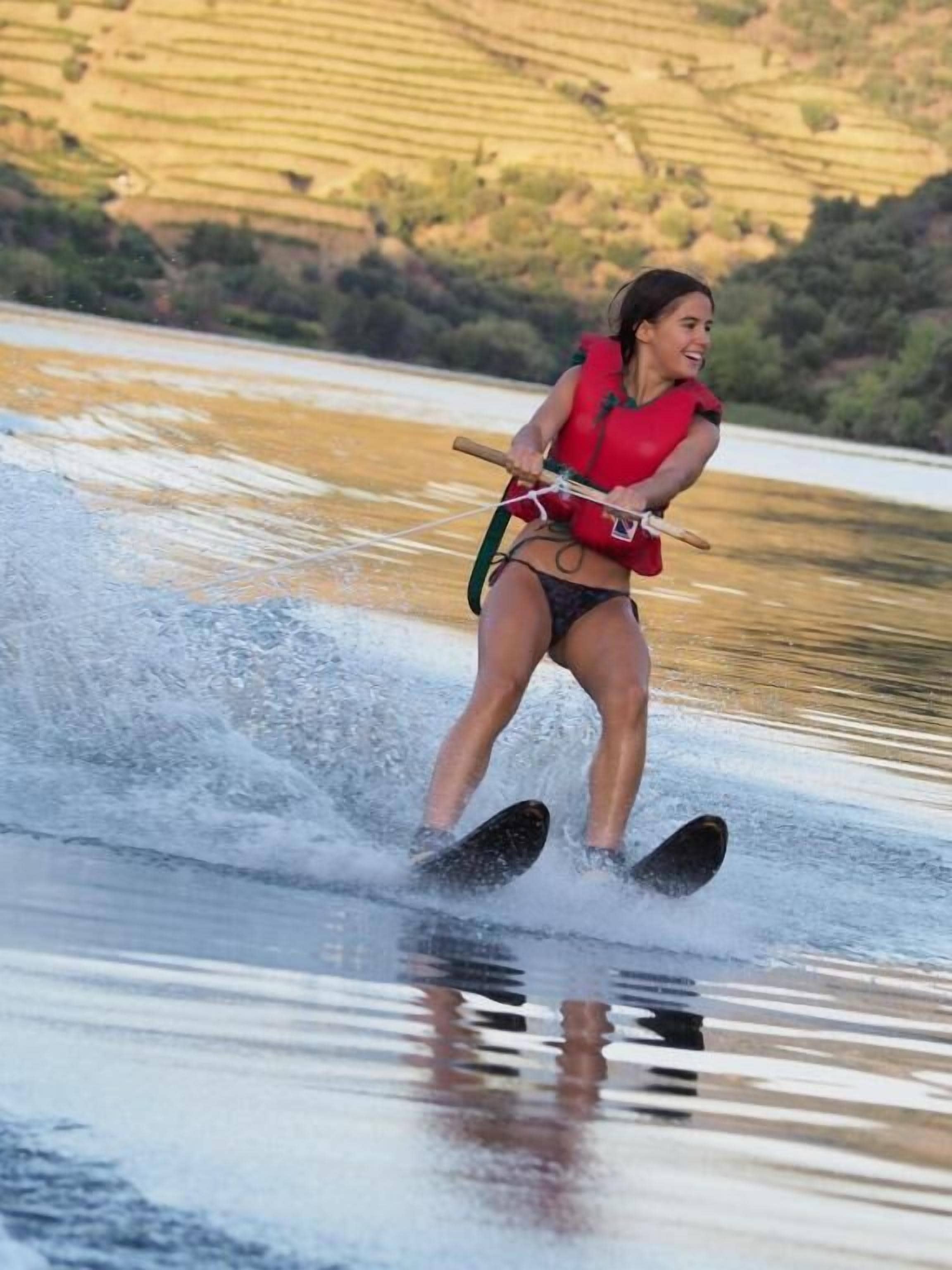 A person water skiing on a calm body of water with a hilly landscape in the background.