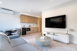 Ein modernes Wohnzimmer mit einer Couch, einem Couchtisch, einem Fernseher und einer Küchenzeile mit Holzschränken und einer Mikrowelle.