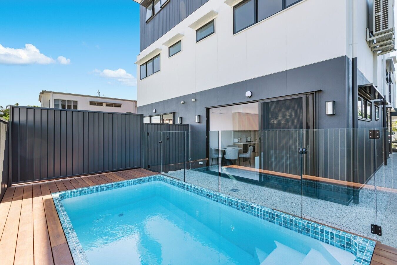A modern building with a swimming pool, a covered patio, and a glass-enclosed entrance.