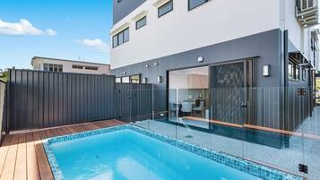 A modern building with a swimming pool, a covered patio, and a glass-enclosed entrance.