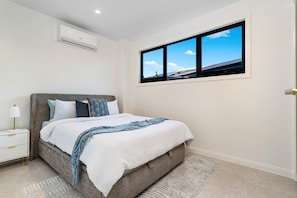 Ein Schlafzimmer mit Bett, Nachttisch, Lampe, Klimaanlage und einem Fenster mit Aussicht.