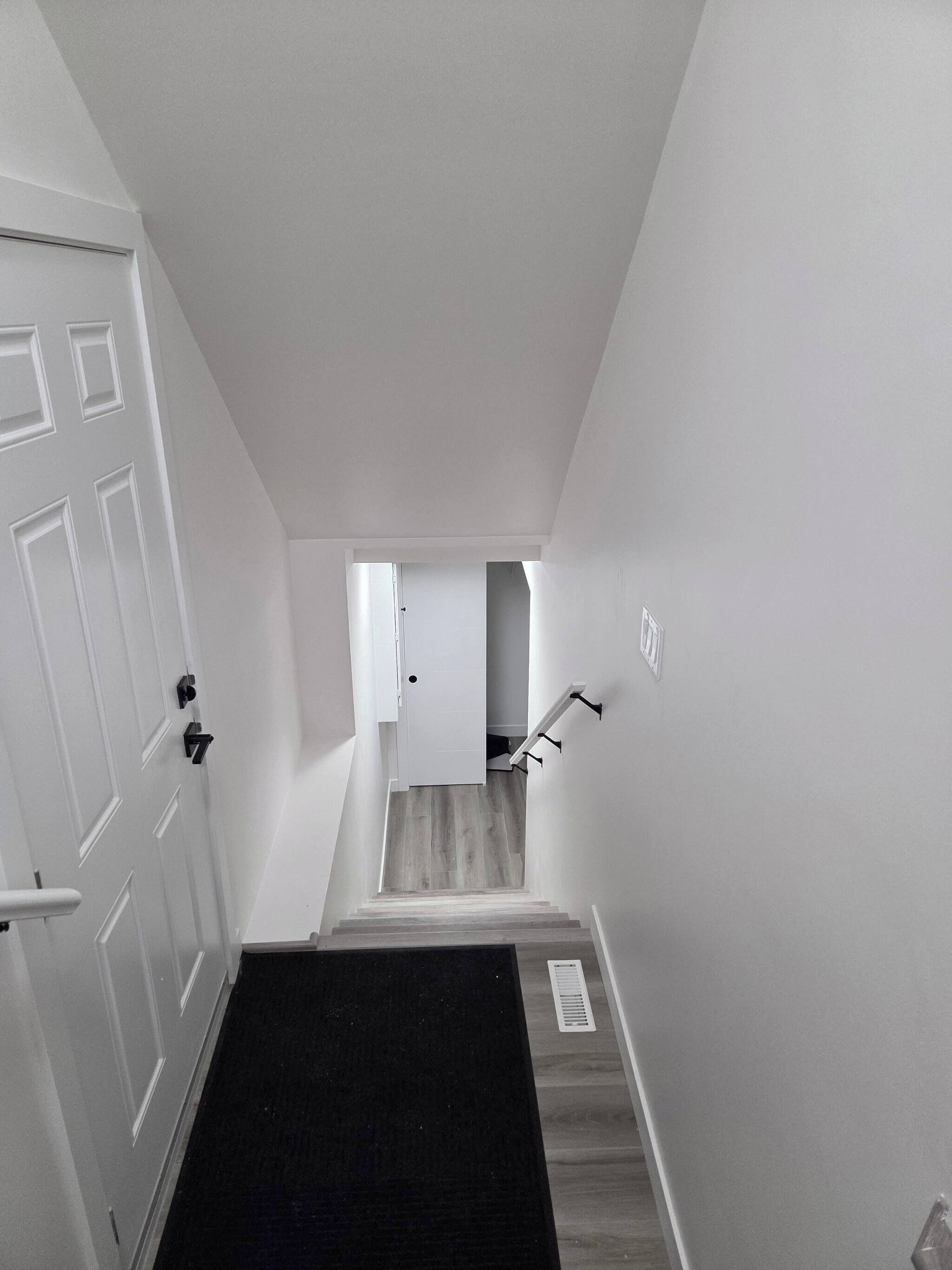 A staircase leading to an upper floor with a door at the top, a handrail on the right, and a black carpeted landing.