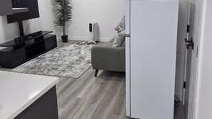 A modern kitchen with a built-in oven, a white refrigerator, and a grey sofa. - The Cozy Corner Home (Winnipeg)